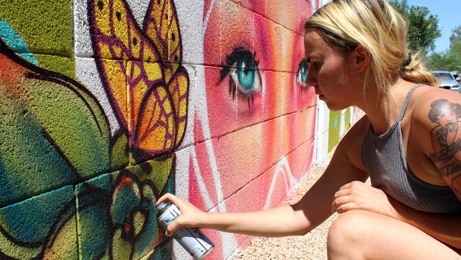 Nyla Lee agrega detalles a una flor en un mural para el patio trasero de una casa. Algunos de sus murales m á s grandes se pueden encontrar en el centro de Phoenix.