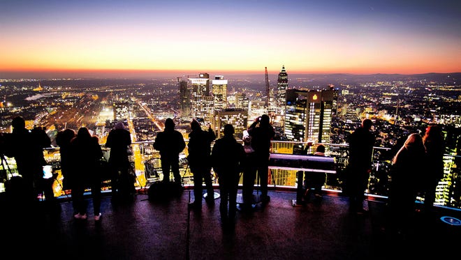 Los turistas se paran en la cima de la torre principal y miran la ciudad de Frankfurt, Alemania, despu é s del atardecer del viernes 16 de noviembre de 2018.
