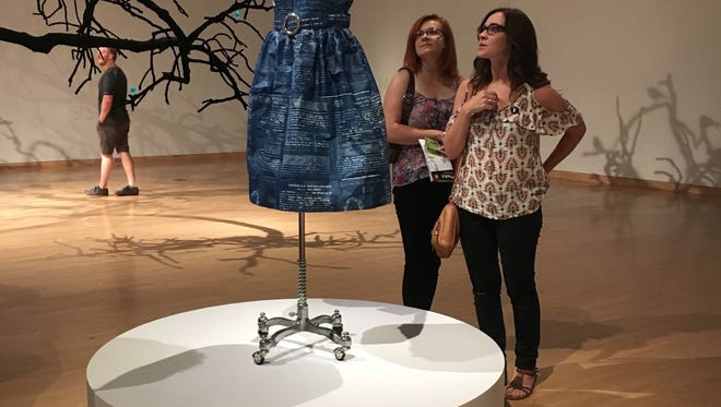 Museum patrons check out local Annie Lopez's "Naturalized Citizens" at the Phoenix Art Museum on July 6, 2018. Lopez crafted the dress out of tamale papers printed with her family's naturalization documents.