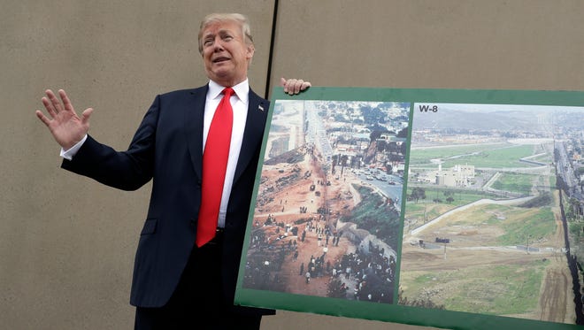 Trump posa frente uno de los prototipos del muro fronterizo, al mismo tiempo que muestra una gráfica en donde se aprecia cómo quedará la obra.