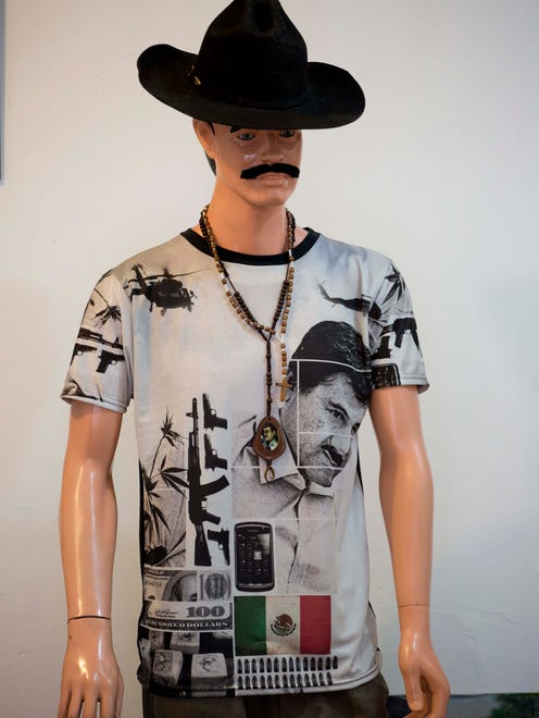 Este otro maniquí que se parece a Joan Sebastian exhibe una camiseta de "narco junior" con el estampado del rostro de Joaquín Loera, y una bandera de México.
