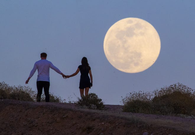 Clint and Kaylee Frazier walk over a hill as a "Super Flower Moon" rises over Fountain Hills on May 6, 2020. The "Flower Moon" is the last in a series of four supermoons in quick succession this year and gets its name from the large number of flowers that bloom this month.
