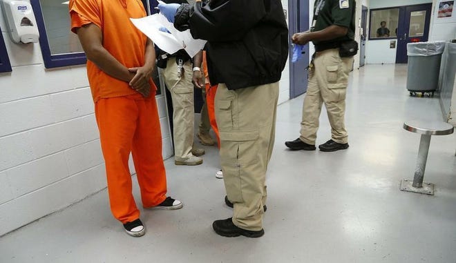 En esta imagen del 24 de septiembre de 2015 se ve un detenido en uniforme naranja siendo procesado por un guardia dentro del Centro de Detención Krome, en Miami.