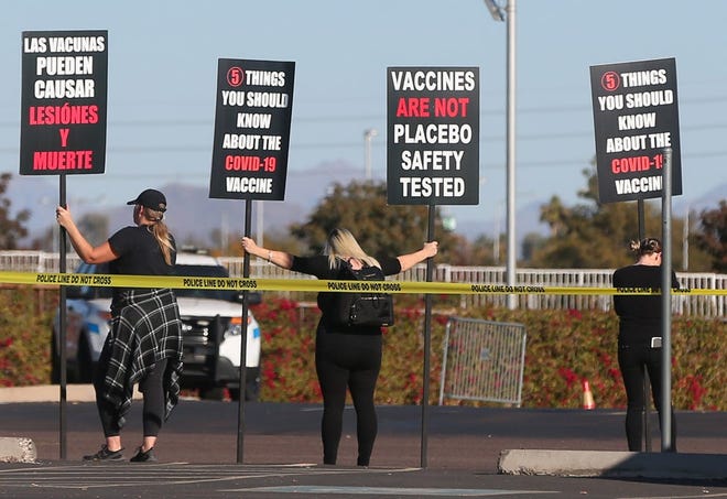 Los manifestantes sostienen carteles en el primer sitio de vacunación COVID-19 24/7 del estado el 11 de enero de 2021, en el State Farm Stadium en Glendale.