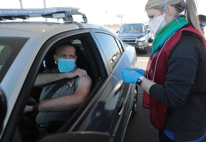 El oficial del DPS de Arizona Jason Davis se arremanga antes de recibir su vacuna COVID-19 en el primer sitio de vacunación COVID-19 24/7 del estado el 11 de enero en el estacionamiento del State Farm Stadium en Glendale, Arizona.