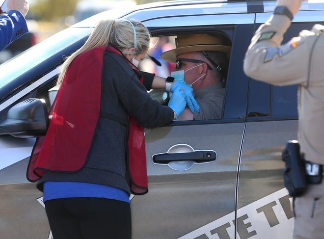 Un trabajador da una vacuna COVID-19 a un oficial del DPS de Arizona durante una prueba en el primer sitio de vacunación COVID-19 24/7 del estado el 11 de enero en el State Farm Stadium en Glendale, Arizona.