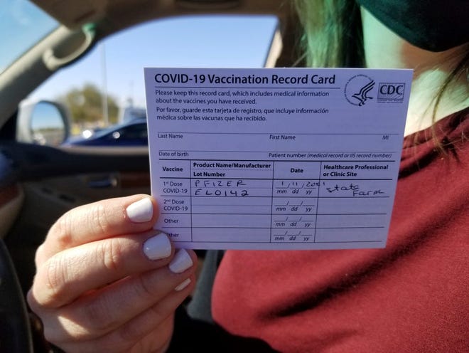 Emily Alexander, de 37 años, muestra su tarjeta de vacunación COVID-19 poco después de recibir la vacuna en el estacionamiento del State Farm Stadium en Glendale, Arizona, el lunes 11 de enero de 2021. El estadio de los Arizona Cardinals abrió el sitio como vacunación el lunes que operará 24/7.