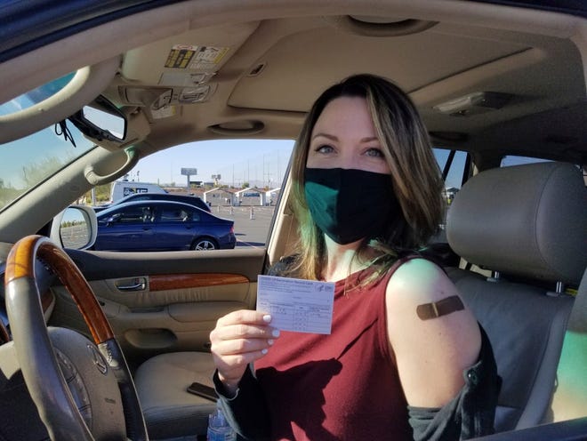 Emily Alexander, de 37 años, muestra su tarjeta de vacunación COVID-19 poco después de recibir la vacuna en el estacionamiento del State Farm Stadium en Glendale, Arizona, el lunes 11 de enero de 2021. El estadio de los Arizona Cardinals abrió el sitio como vacunación el lunes que operará 24/7.
